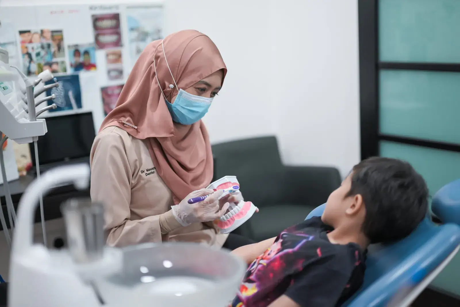 A dentist at Mawarni Dental Clinic explaining treatment to a young patient